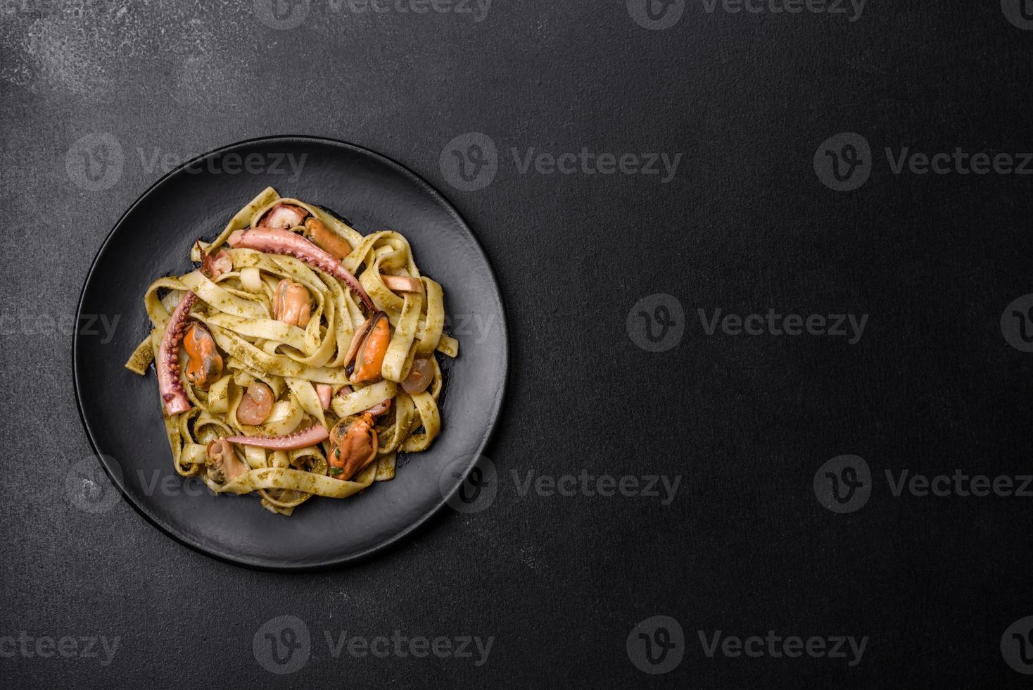 Delicious fresh pasta with pesto sauce and seafood on a black plate photo