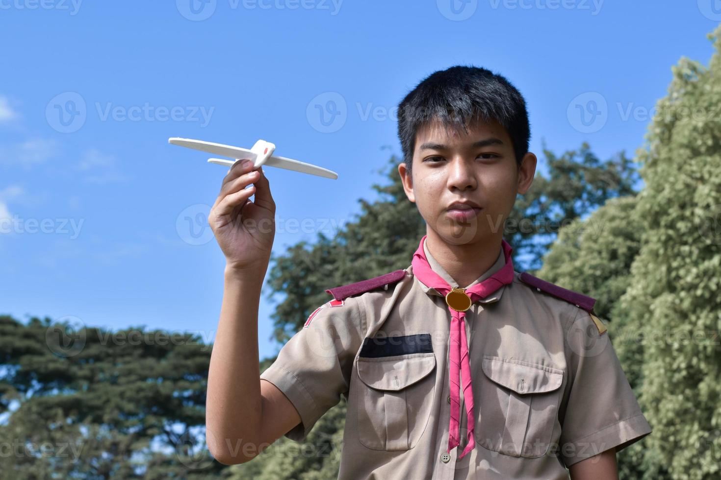 el boy scout asiático sostiene un modelo de avión blanco contra un fondo nublado y azul, enfoque suave y selectivo. foto