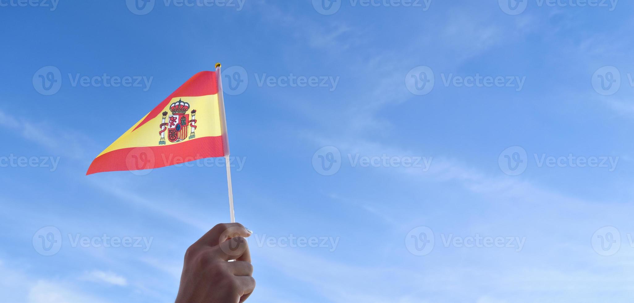 Spanish national flag or Spain flag holding in hand and waving on blue sky background, soft and selective focus. photo