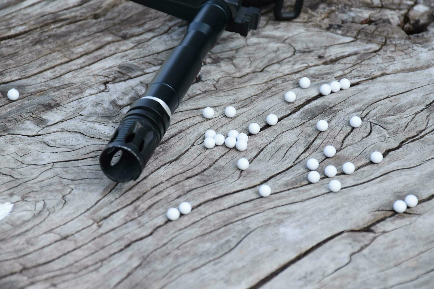 BB gun or airsoft gun muzzle and white bullets on wooden plank, soft and selective focus. photo