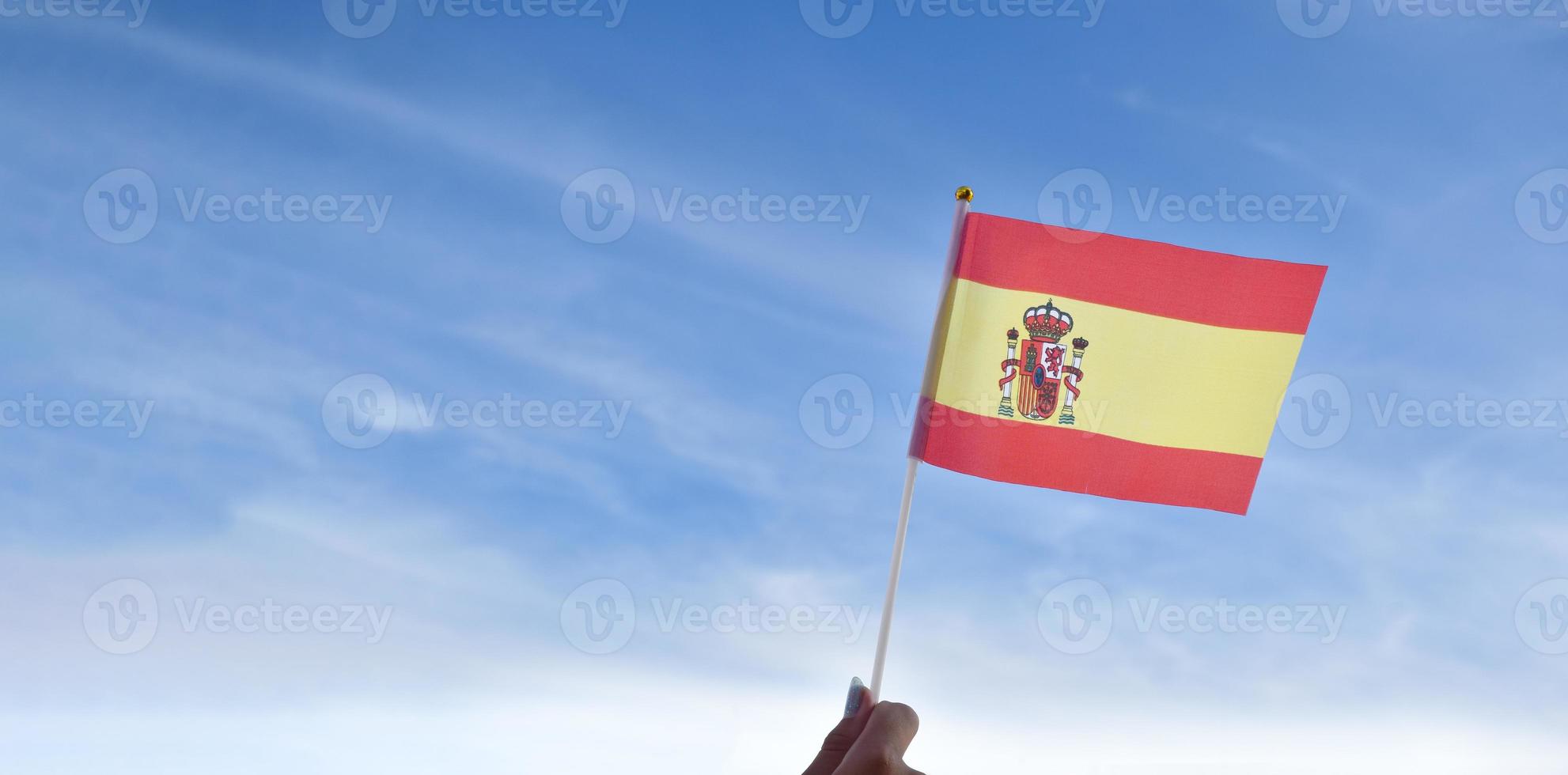 Spanish national flag or Spain flag holding in hand and waving on blue sky background, soft and selective focus. photo
