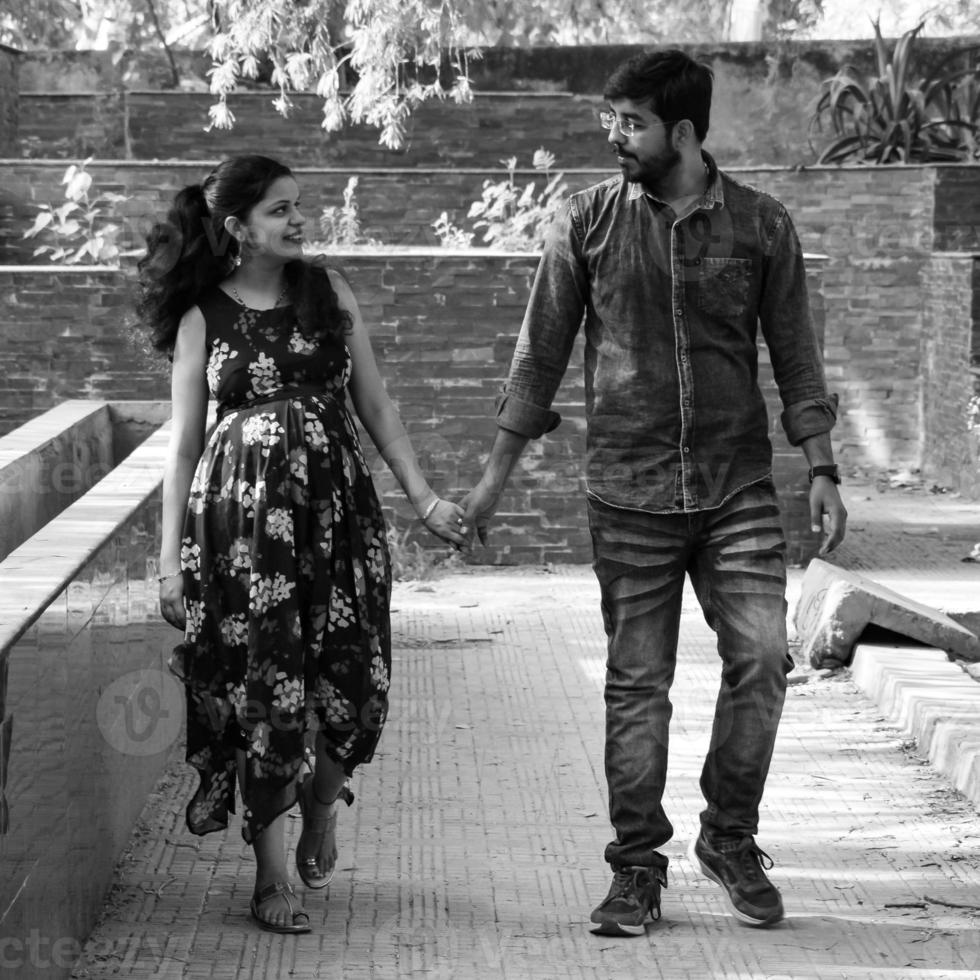 Indian couple posing for maternity baby shoot. The couple is posing in a lawn with green grass and the woman is falunting her baby bump in Lodhi Garden in New Delhi, India photo