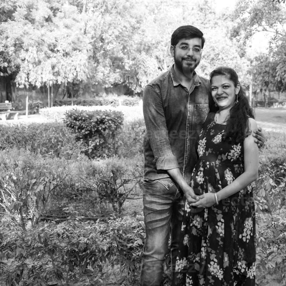 Indian couple posing for maternity baby shoot. The couple is posing in a lawn with green grass and the woman is falunting her baby bump in Lodhi Garden in New Delhi, India photo