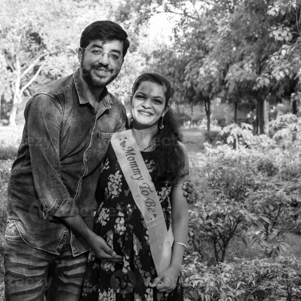 Indian couple posing for maternity baby shoot. The couple is posing in a lawn with green grass and the woman is falunting her baby bump in Lodhi Garden in New Delhi, India photo