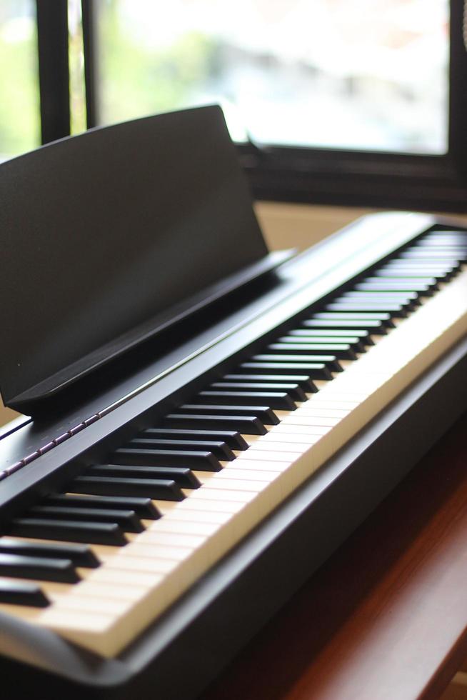 Black piano keyboard with white keys against window interior background photo