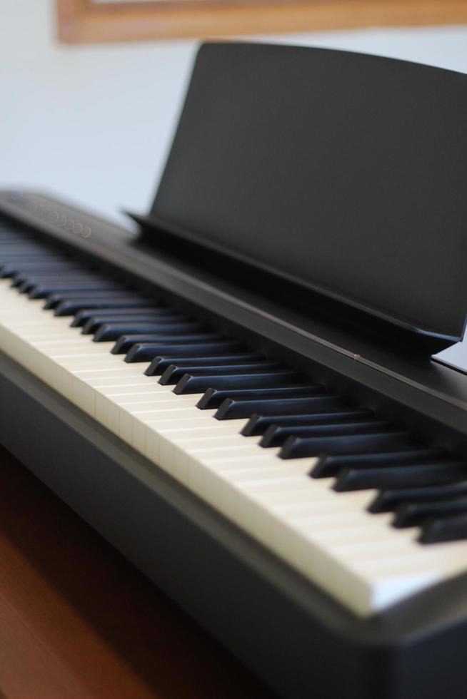 Black piano keyboard with white keys against window interior background photo
