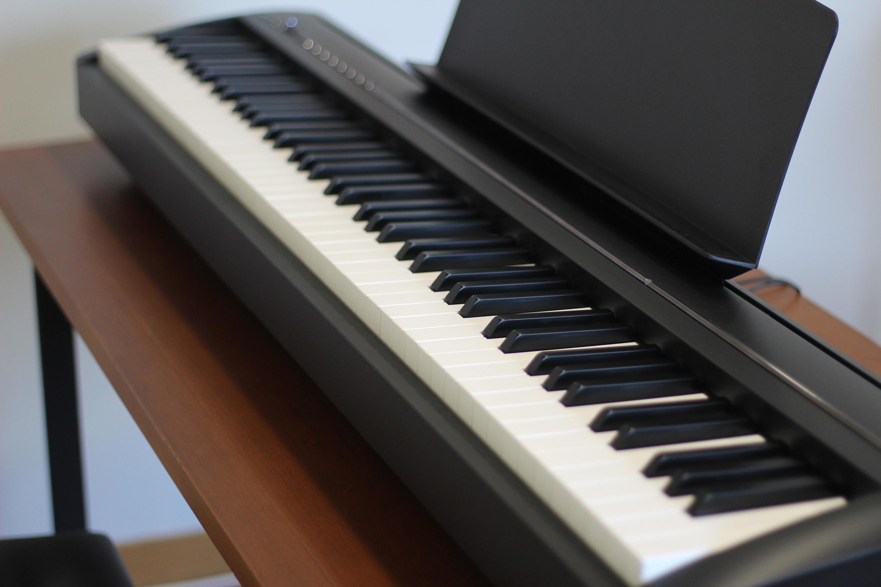 Black piano keyboard with white keys against window interior background