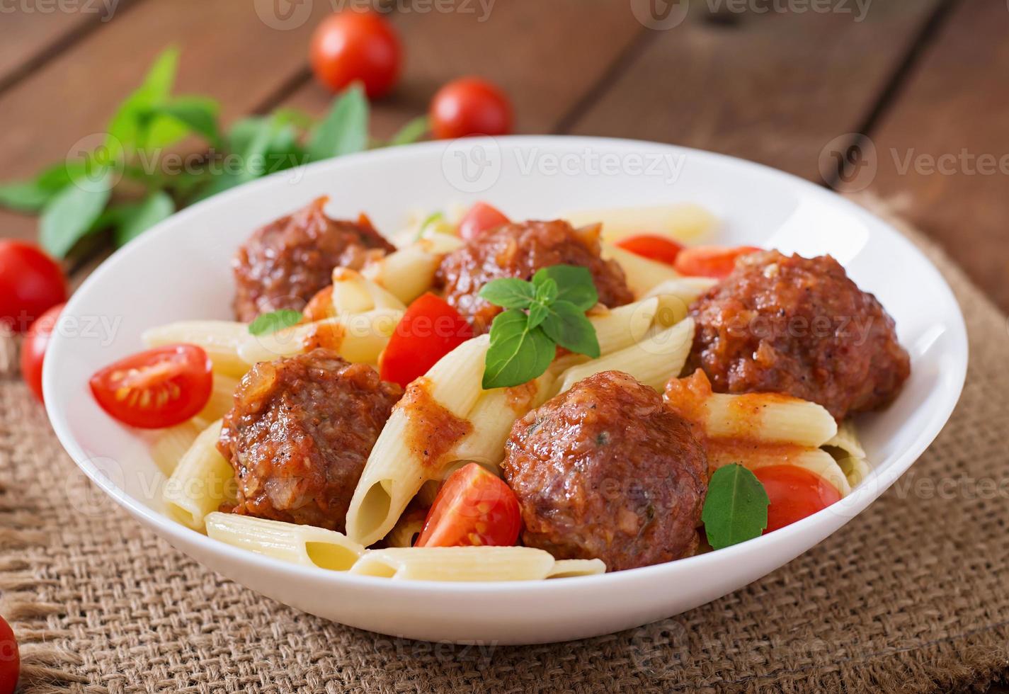 Penne pasta with meatballs in tomato sauce in a white bowl photo