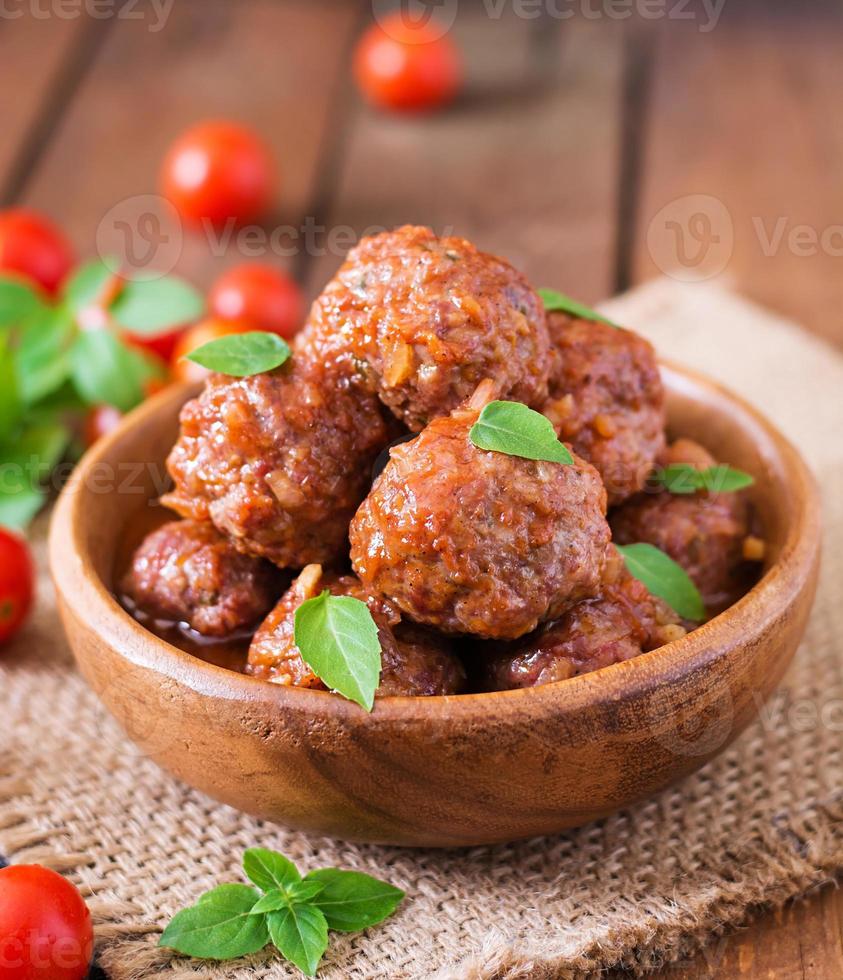 Meatballs in sweet and sour tomato sauce and basil in a wooden bowl photo