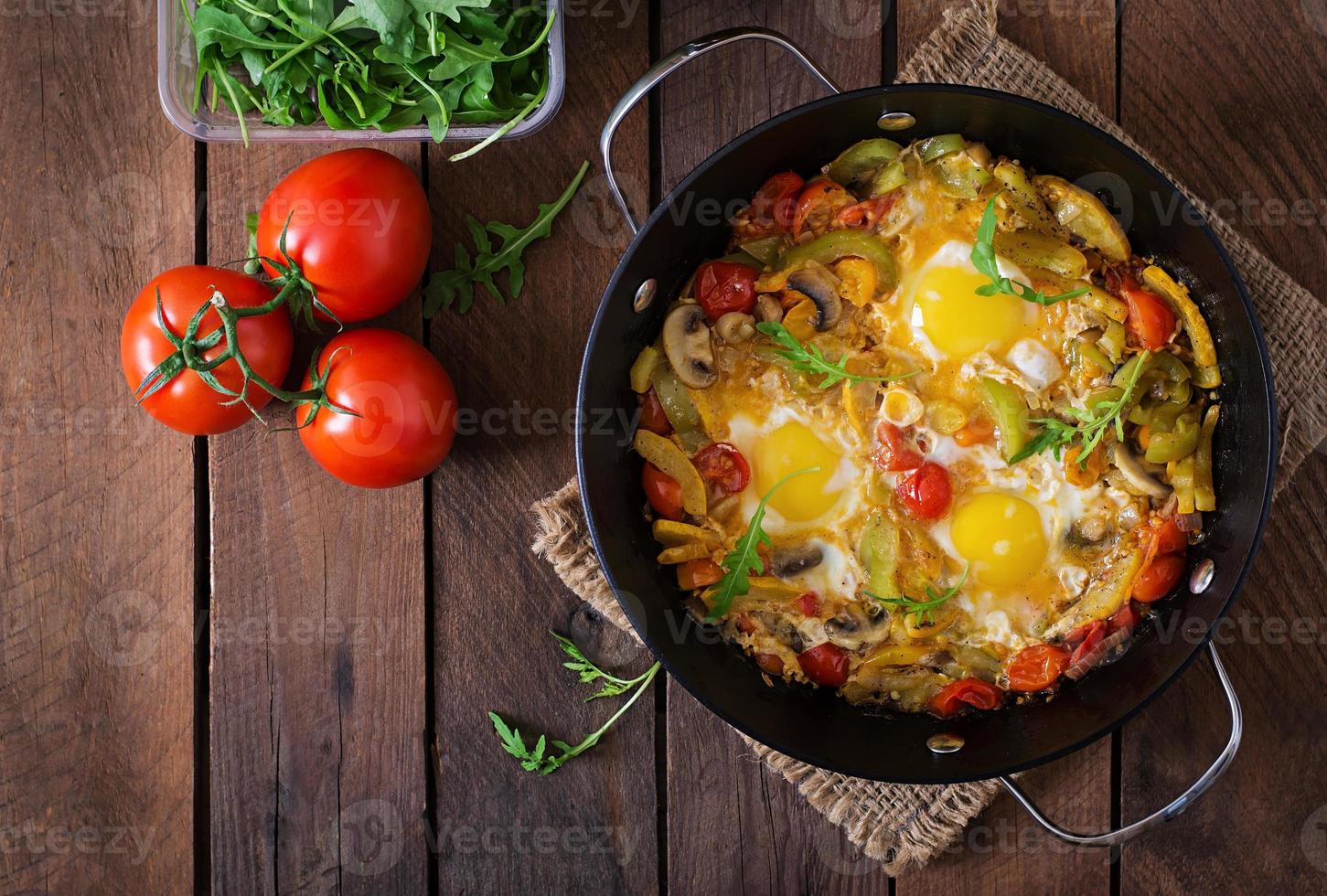 Fried eggs with vegetables in a frying pan on a wooden background photo