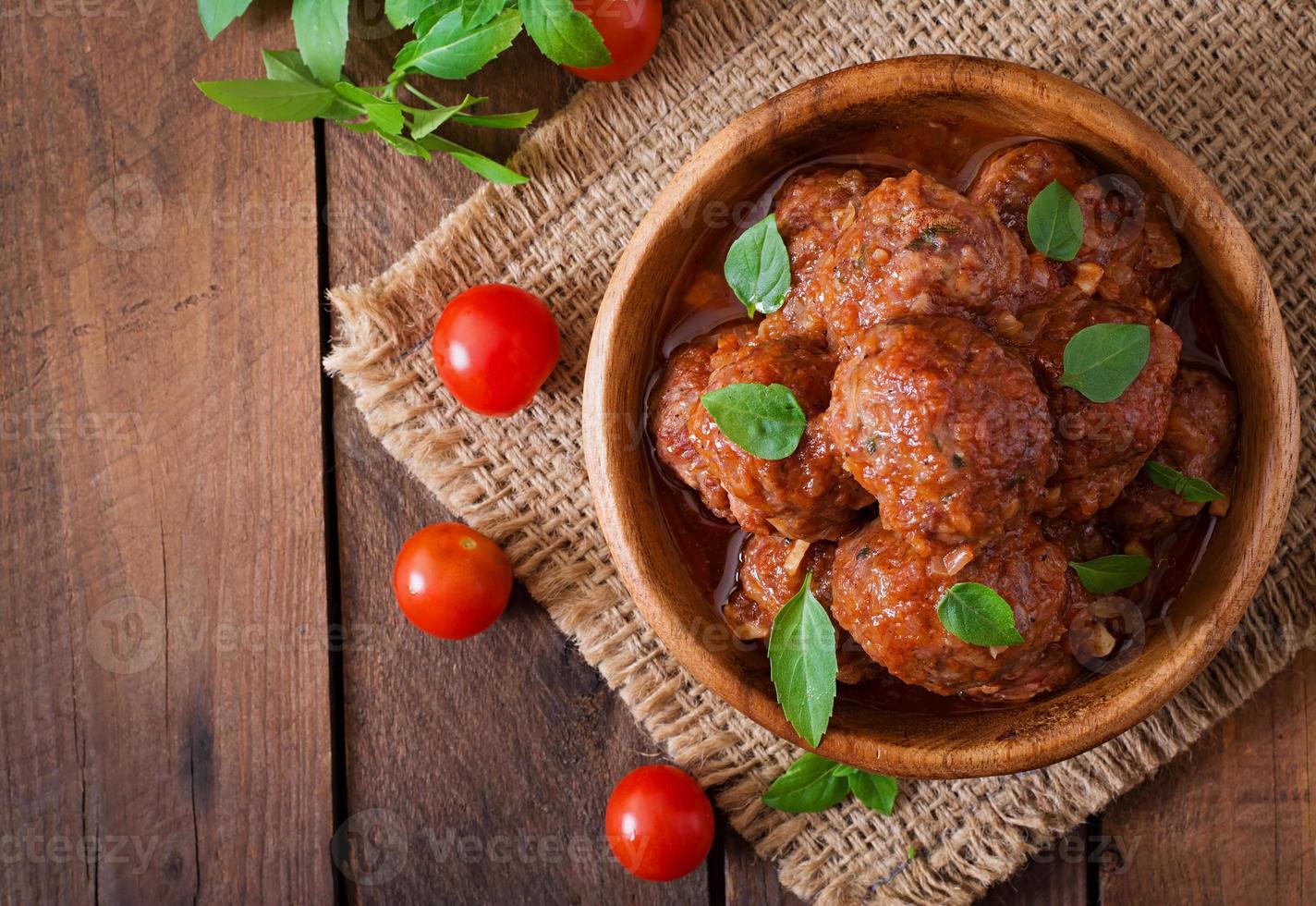 Meatballs in sweet and sour tomato sauce and basil in a wooden bowl photo