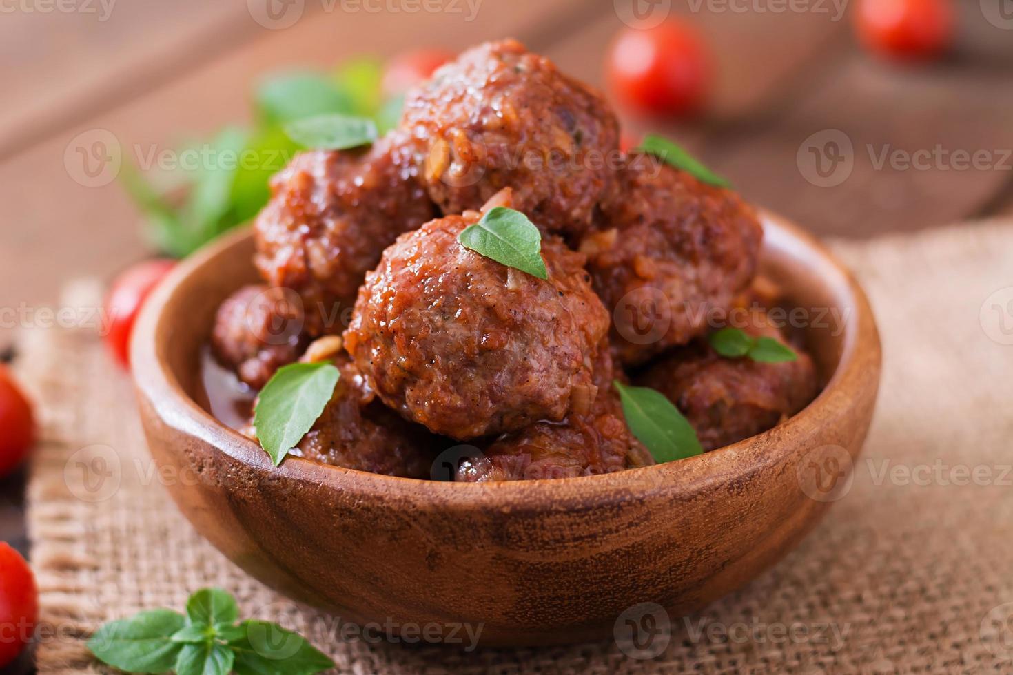 Meatballs in sweet and sour tomato sauce and basil in a wooden bowl photo