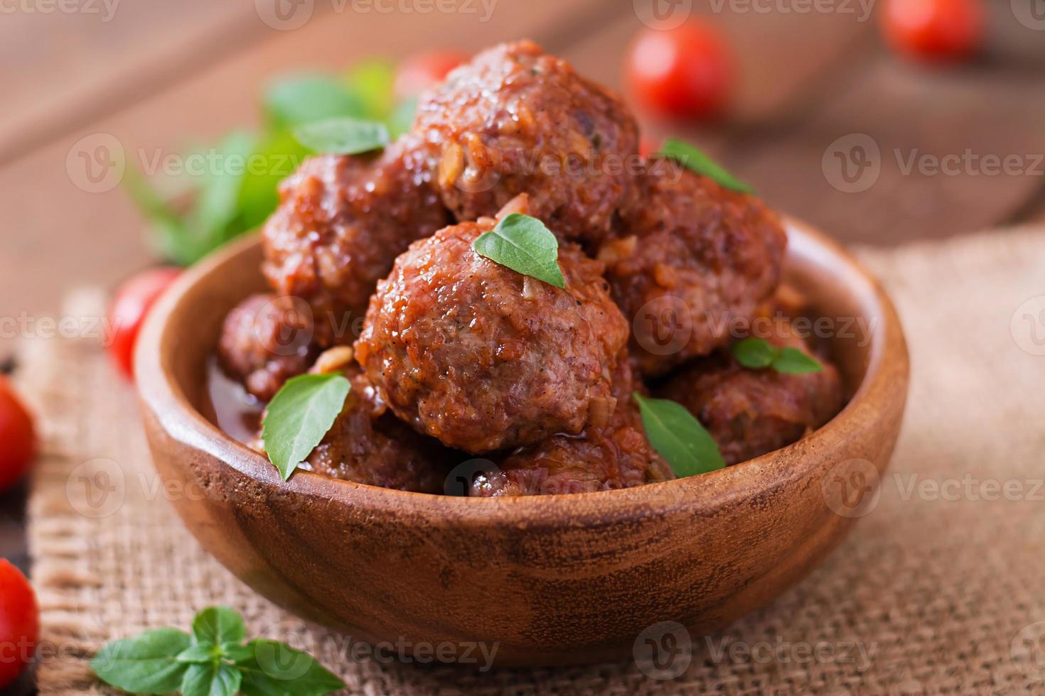 albóndigas en salsa de tomate agridulce y albahaca en un bol de madera foto