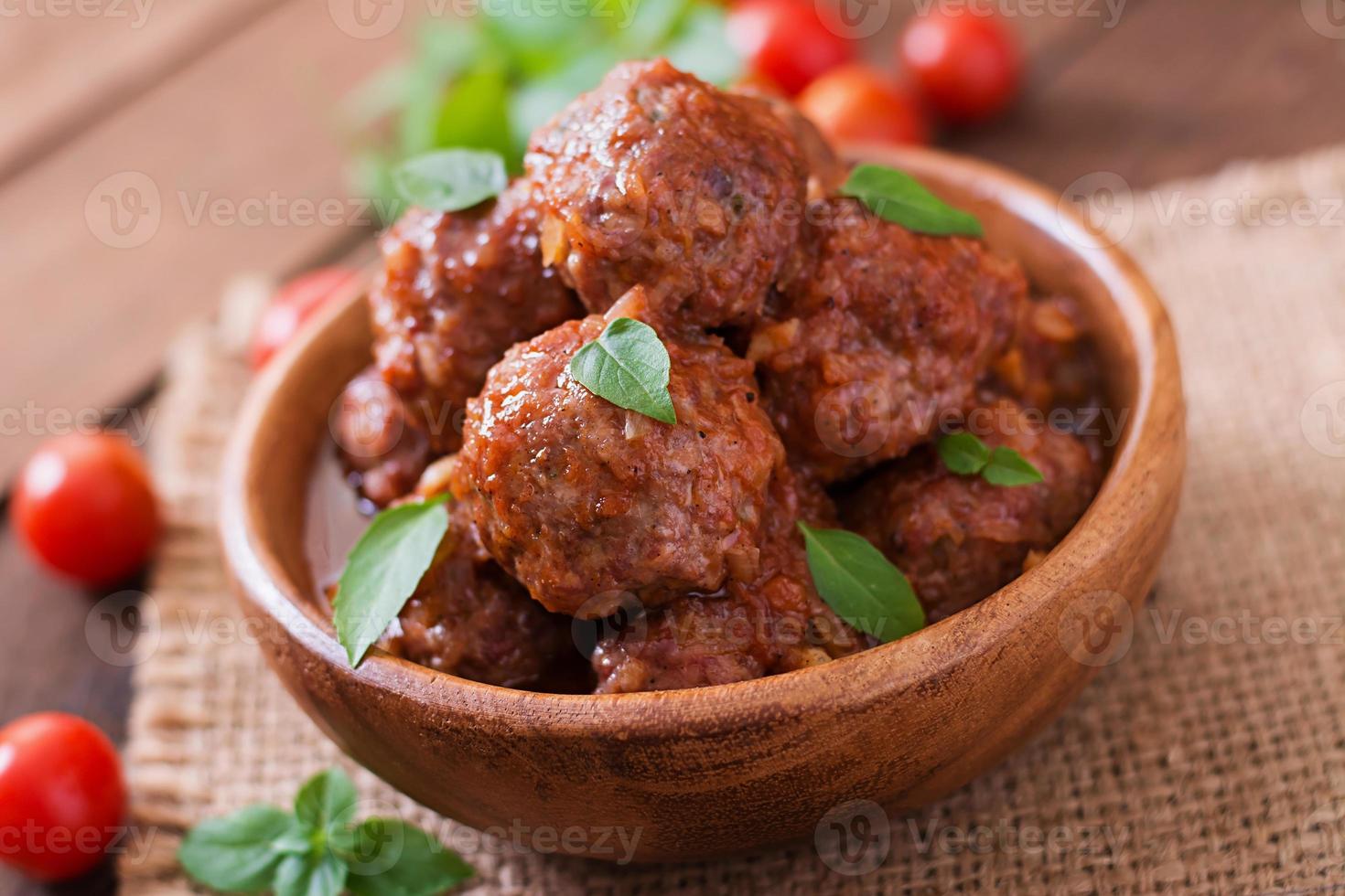 Meatballs in sweet and sour tomato sauce and basil in a wooden bowl photo