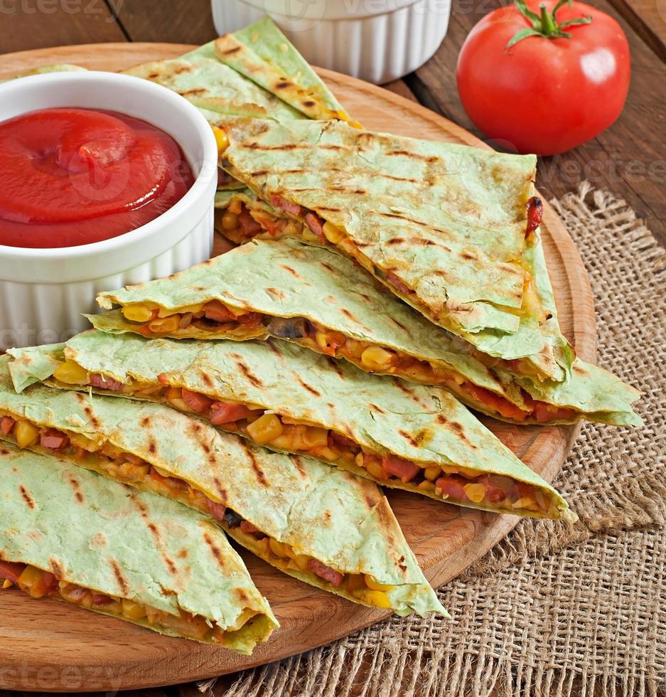 Mexican Quesadilla sliced with vegetables and sauces on the table photo