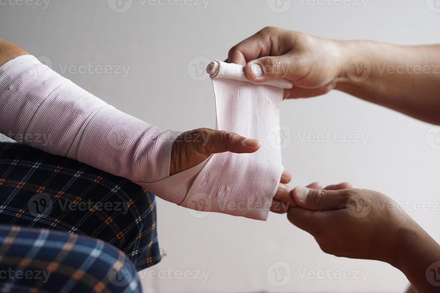 cierre las manos envolviendo la muñeca torcida del paciente con una venda elástica. concepto, primeros auxilios y tratamiento de lesiones en el brazo. accidente. seguro. foto