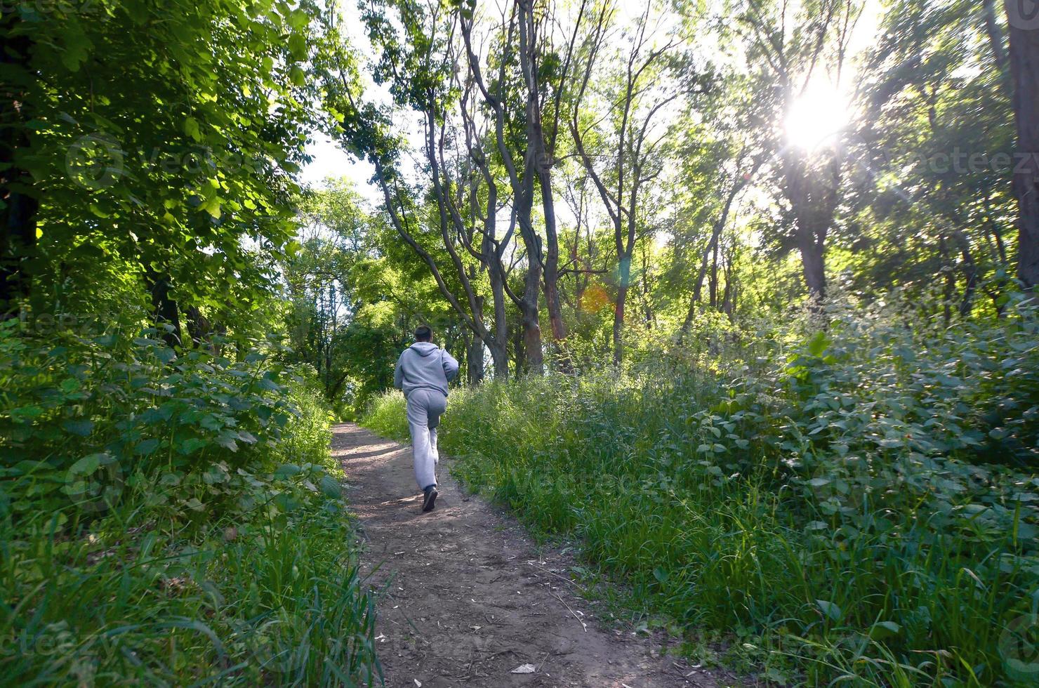 un joven con un traje deportivo gris corre por el camino entre los foto