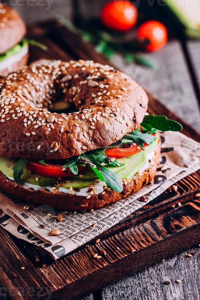 bagels con crema, aguacate, tomates y rúcula sobre tabla de madera. desayuno saludable. foto