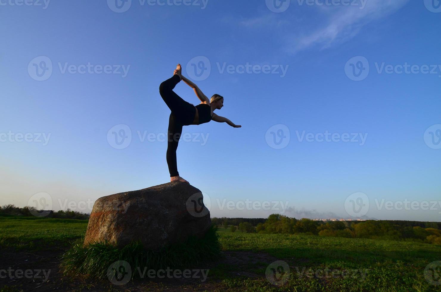 Silhouette of young blonde girl in sport suit practice yoga on a picturesque green hill in the evening at sunset. The concept of exercising and healthy lifestyles photo