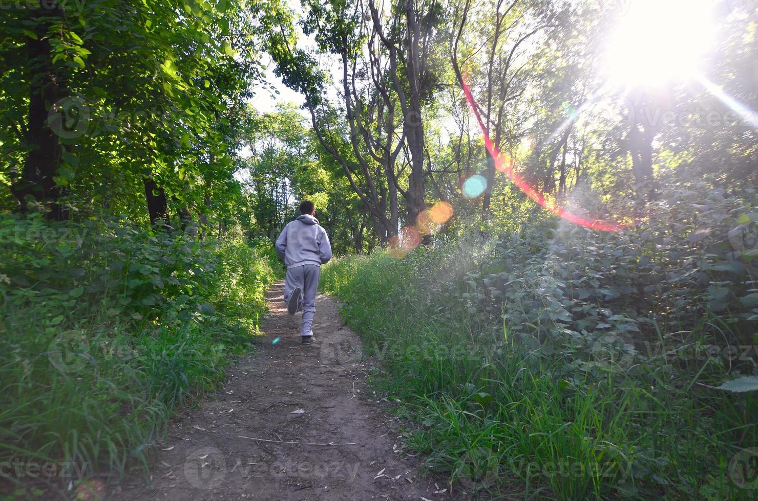 A young guy in a gray sports suit runs along the path among the photo