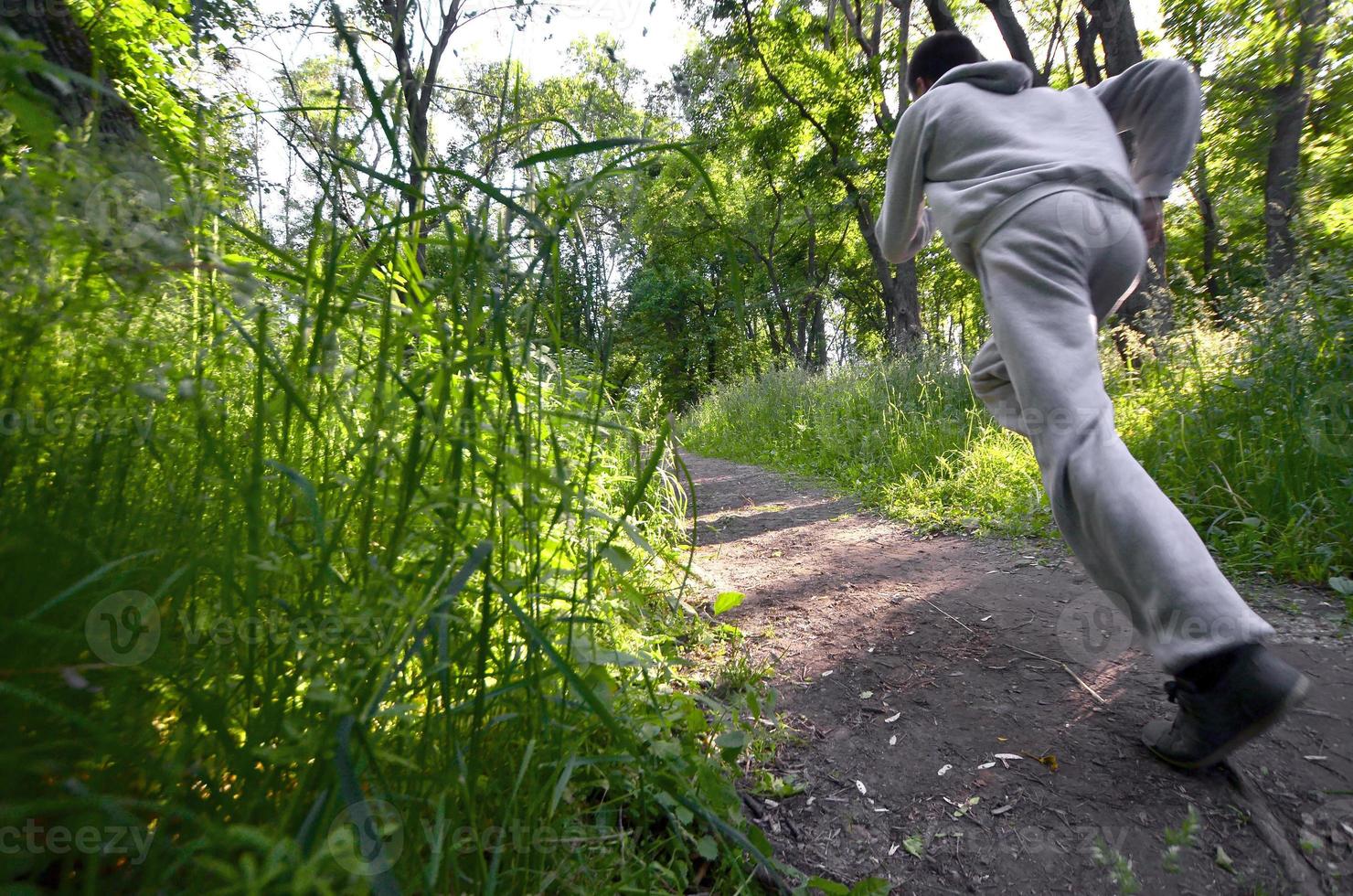 A young guy in a gray sports suit runs along the path among the photo