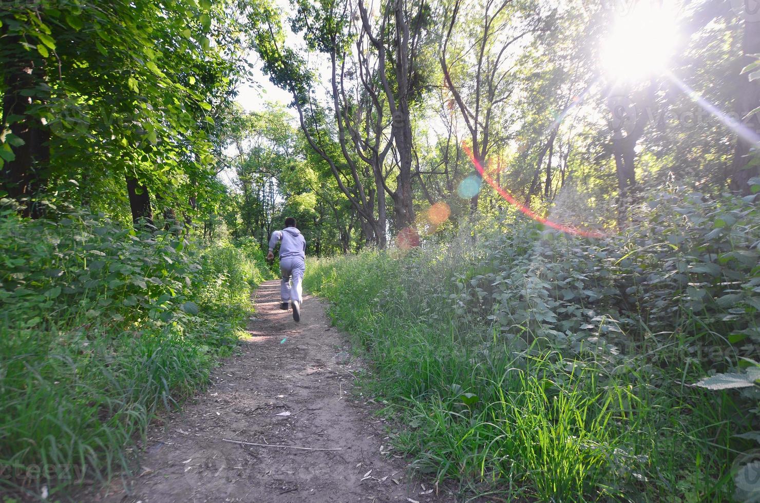 A young guy in a gray sports suit runs along the path among the photo