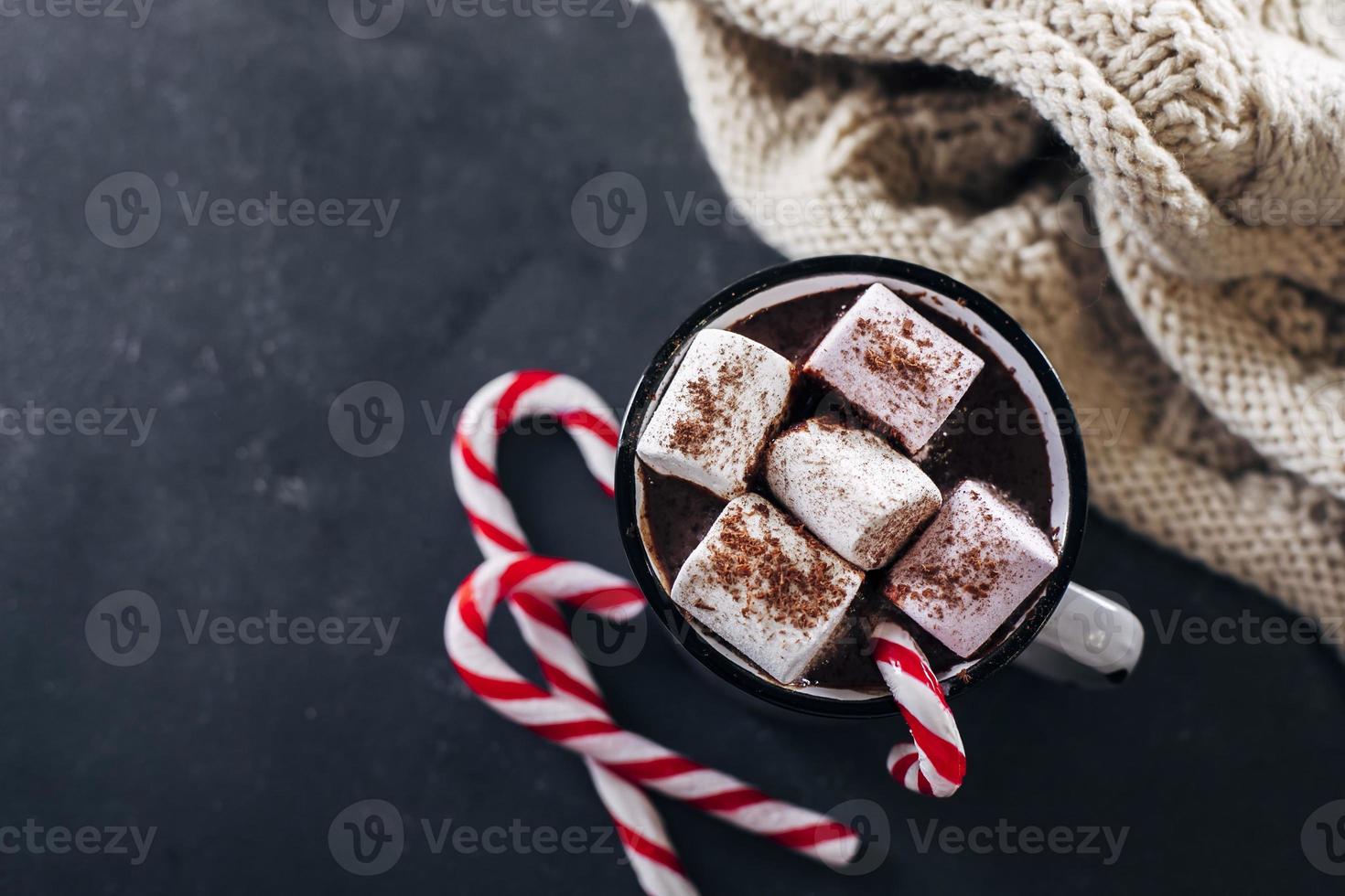 Winter cozy beverage. Glass with hot chocolate with marshmallow, candy cane, cozy scarf. Top view photo