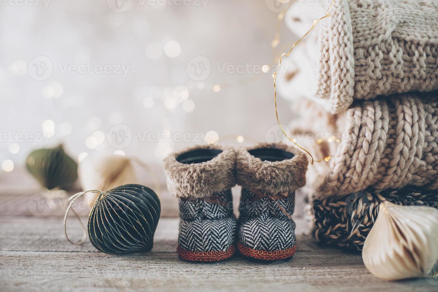 pila de acogedores suéteres de punto de invierno, lindas botas pequeñas y adornos navideños en un fondo borroso con bokeh. foto