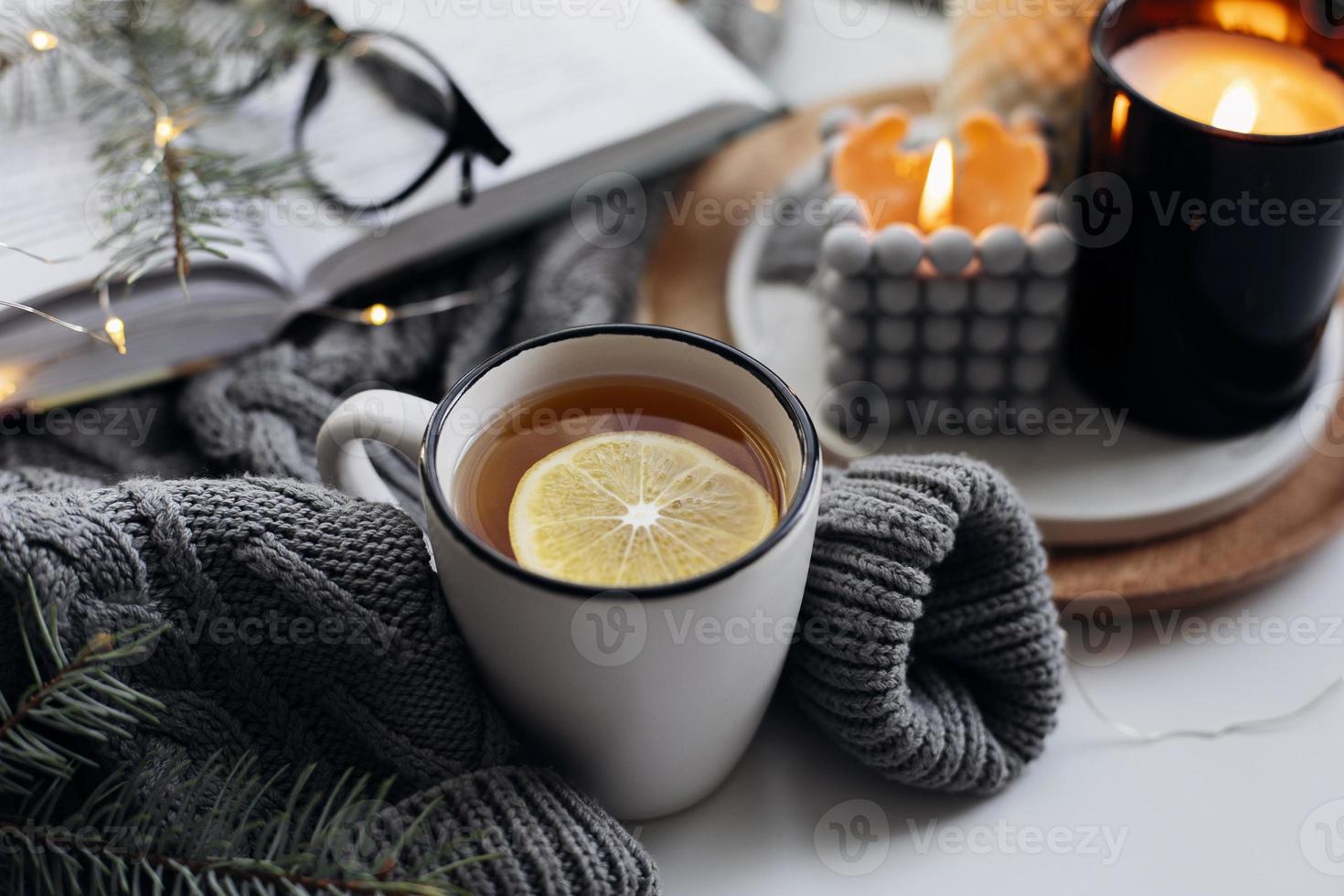 concepto acogedor de casa de invierno. taza con té de limón, libro abierto, suéter cálido, velas y abeto. bienestar, concepto relajante foto