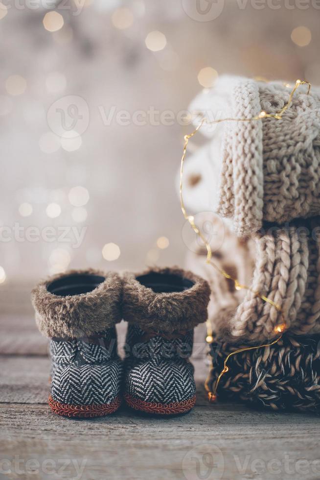 Stack of cozy winter knitted sweaters, cute small boots and christmas ornaments on a blurred background with bokeh. Warm Cozy Concept. Copy space photo