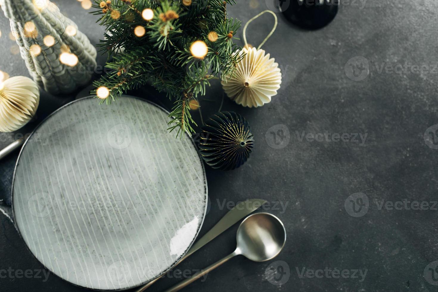 Christmas table setting with empty craft ceramic plate and silver cutlery on dark stone background. Top view. photo