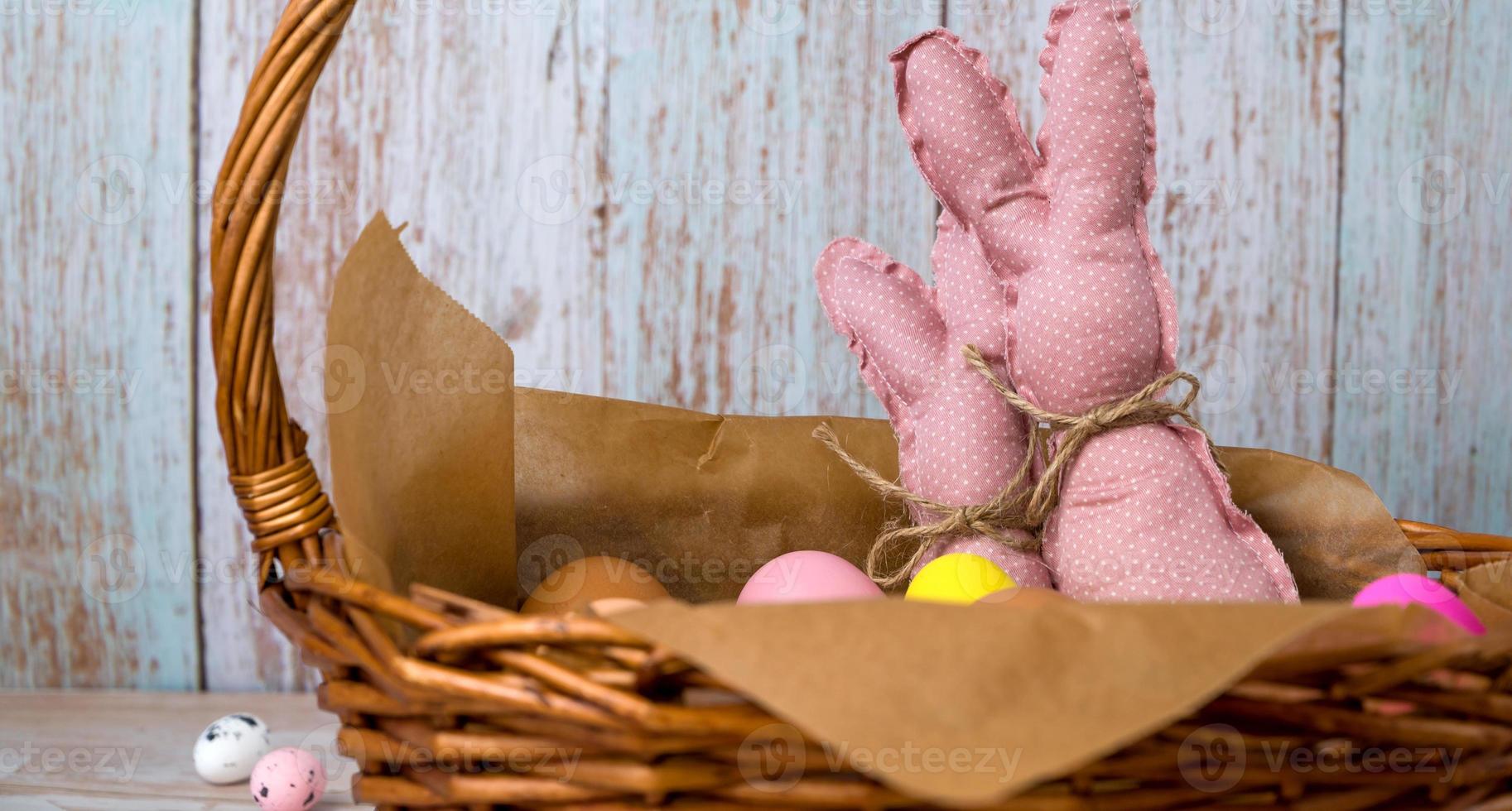 Closeup of pink toy bunnies in the basket full of colorfull eggs. Happy easter banner with place for text photo