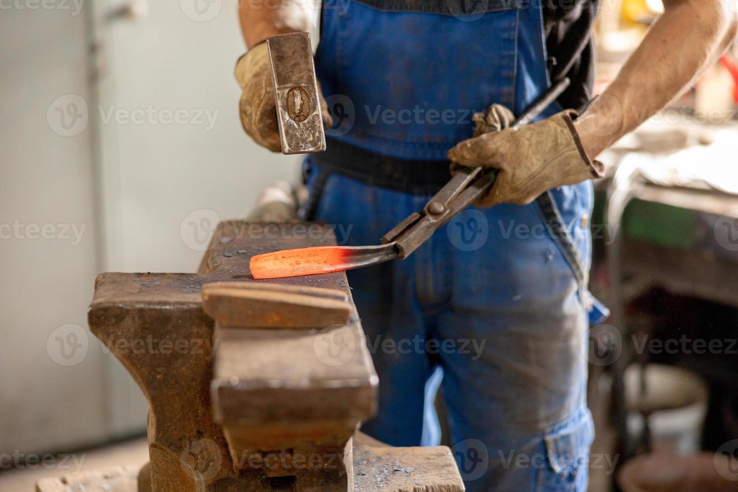 vista de cerca del metal calentado y el yunque. el herrero en el proceso de producción de productos metálicos hechos a mano en la fragua. herrero forjando metal con un martillo. industria metalúrgica, antigua profesión. foto