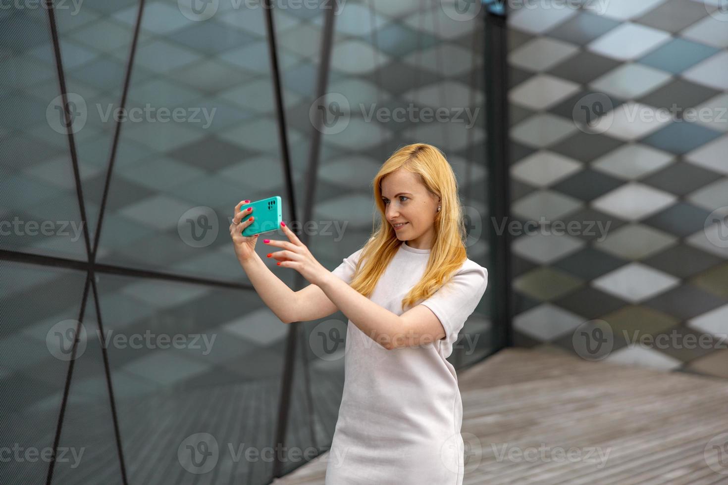 Young blond woman making selfie on smartphone for her followers. Young influencer girl. Popularity in internet, friends online. Beautiful girl making content for her social media account. photo