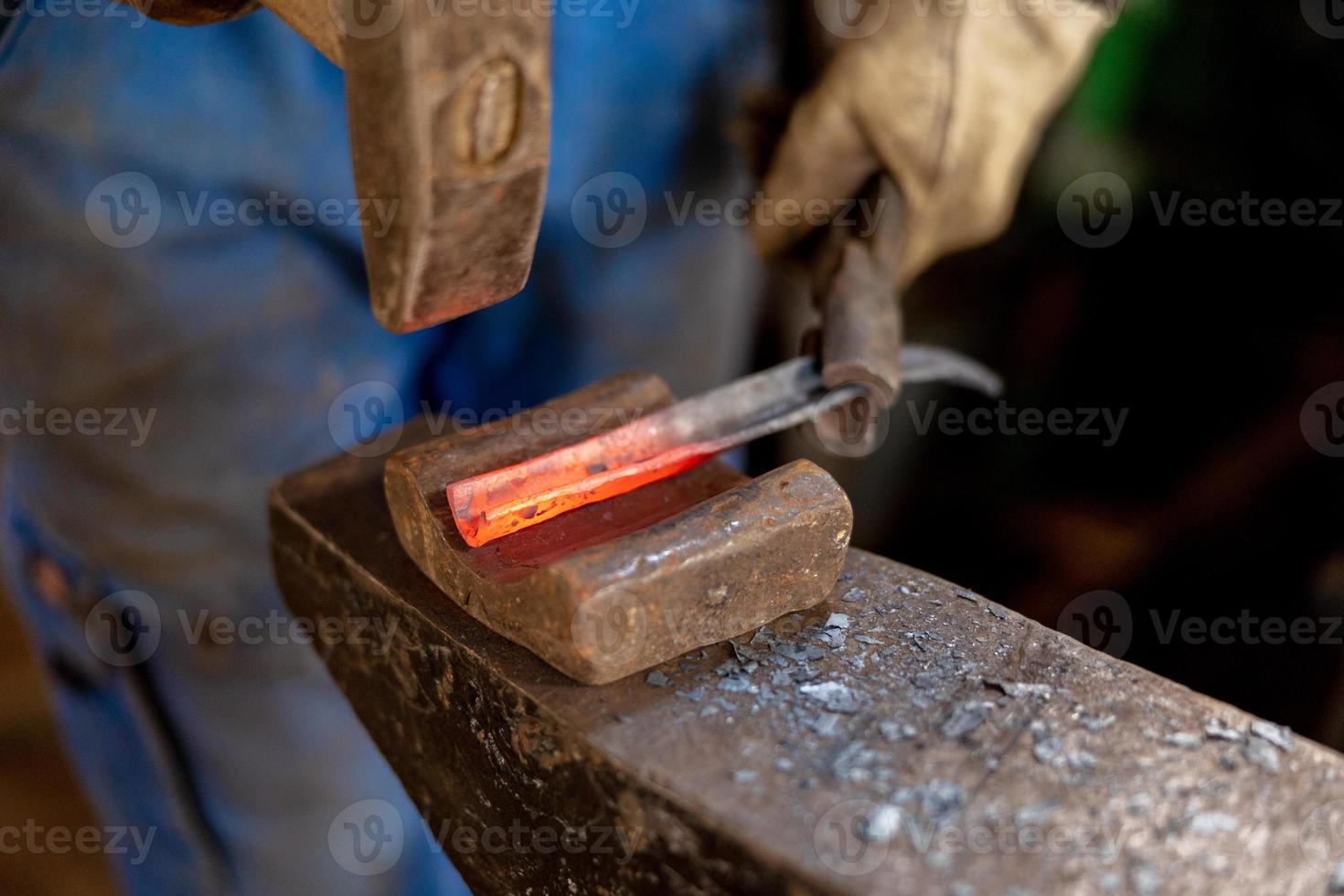 Close up view of heated metal and anvil. The blacksmith in the production process of metal products handmade in the forge. Blacksmith forging metal with a hammer. Metal industry, old profession. photo