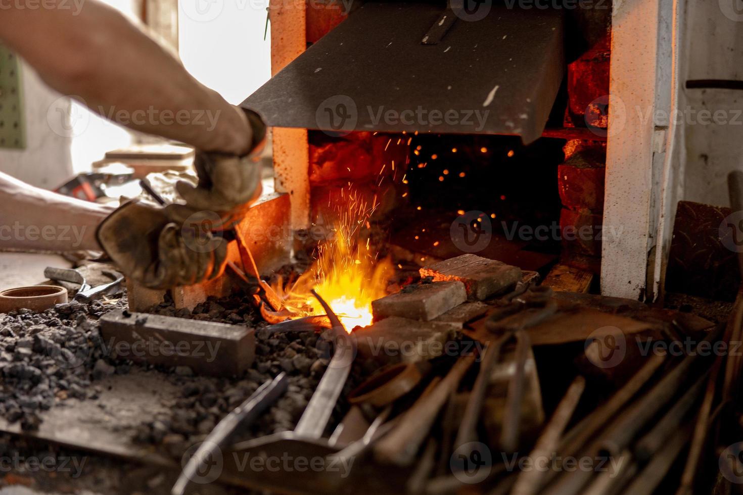 el herrero en proceso de producción de productos metálicos, hechos a mano en la fragua. el artesano calienta el metal en el fuego. industria metalúrgica, antigua profesión. foto