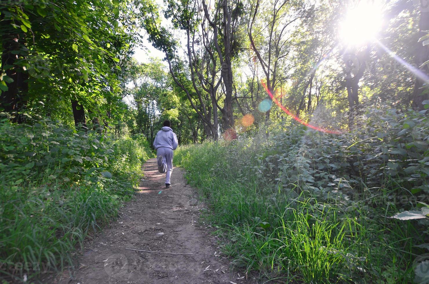 A young guy in a gray sports suit runs along the path among the photo