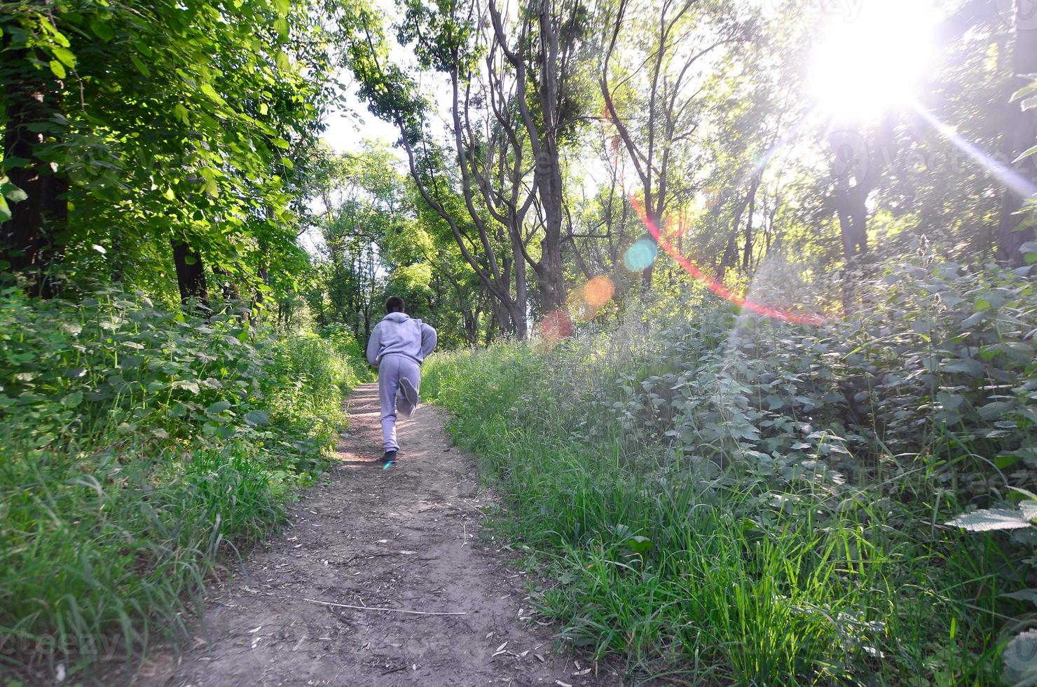 A young guy in a gray sports suit runs along the path among the photo