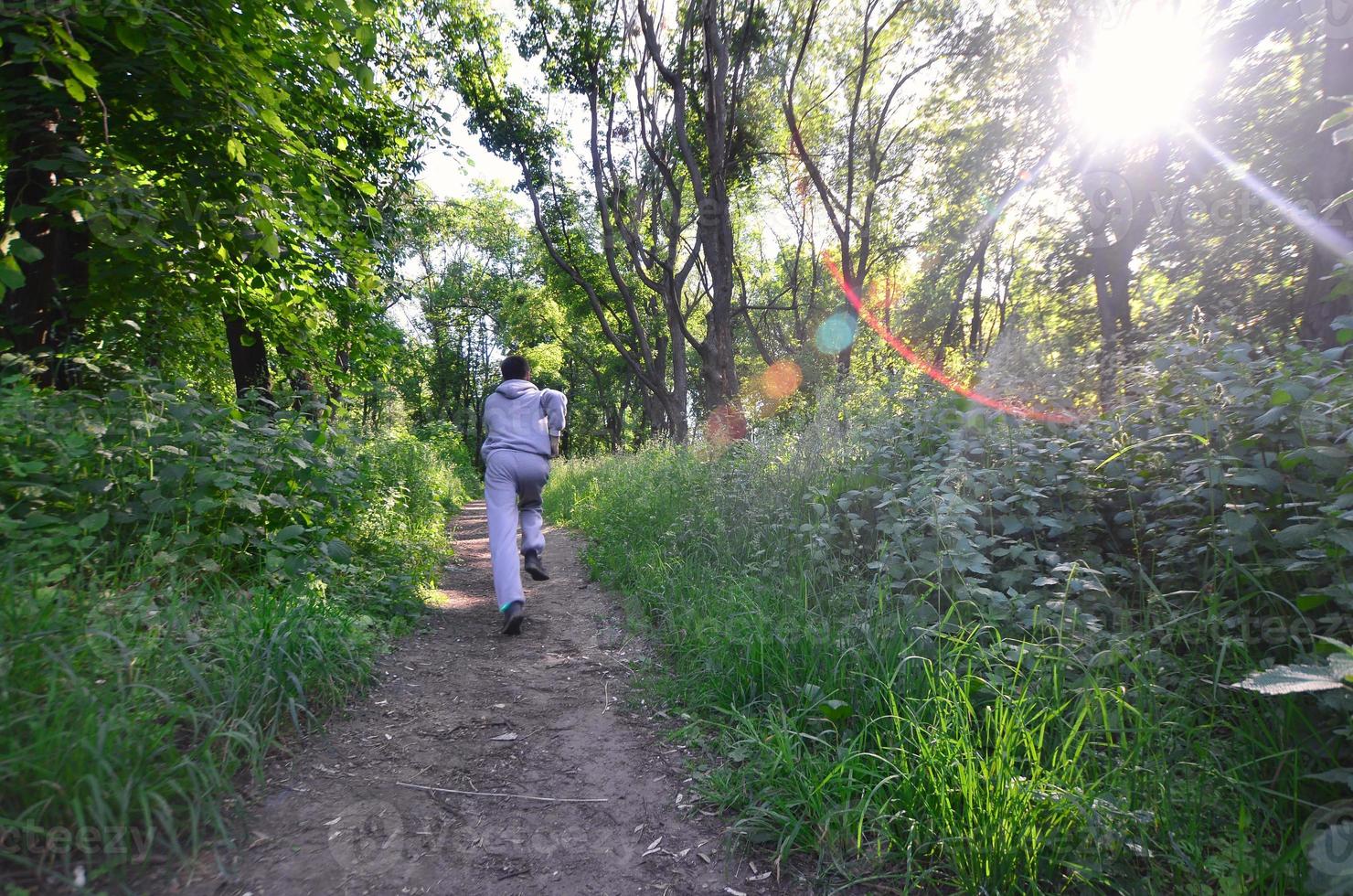 A young guy in a gray sports suit runs along the path among the photo