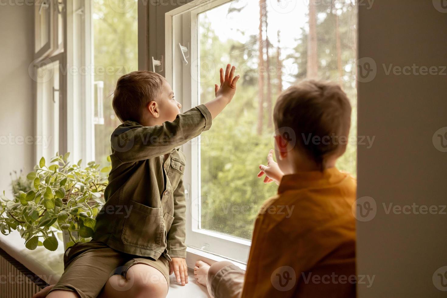 Children sitting on windowsill and waiting for someone comming. Two brothers, friends. Cute preschool kids alone at home. Boys are waiting for their mother or father. Loneliness. Busy parents. photo