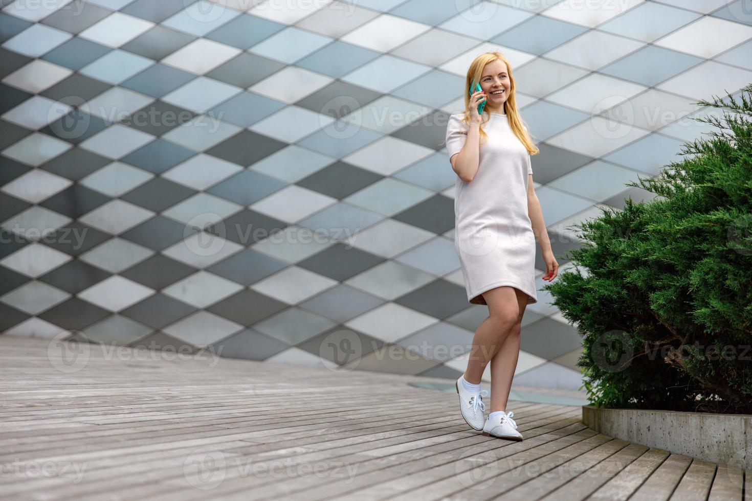 Young blond woman making a call with her smartphone. Girl talking with friends with mobile phone. Leisure activity, communication. Conversation. Mobile technology. photo