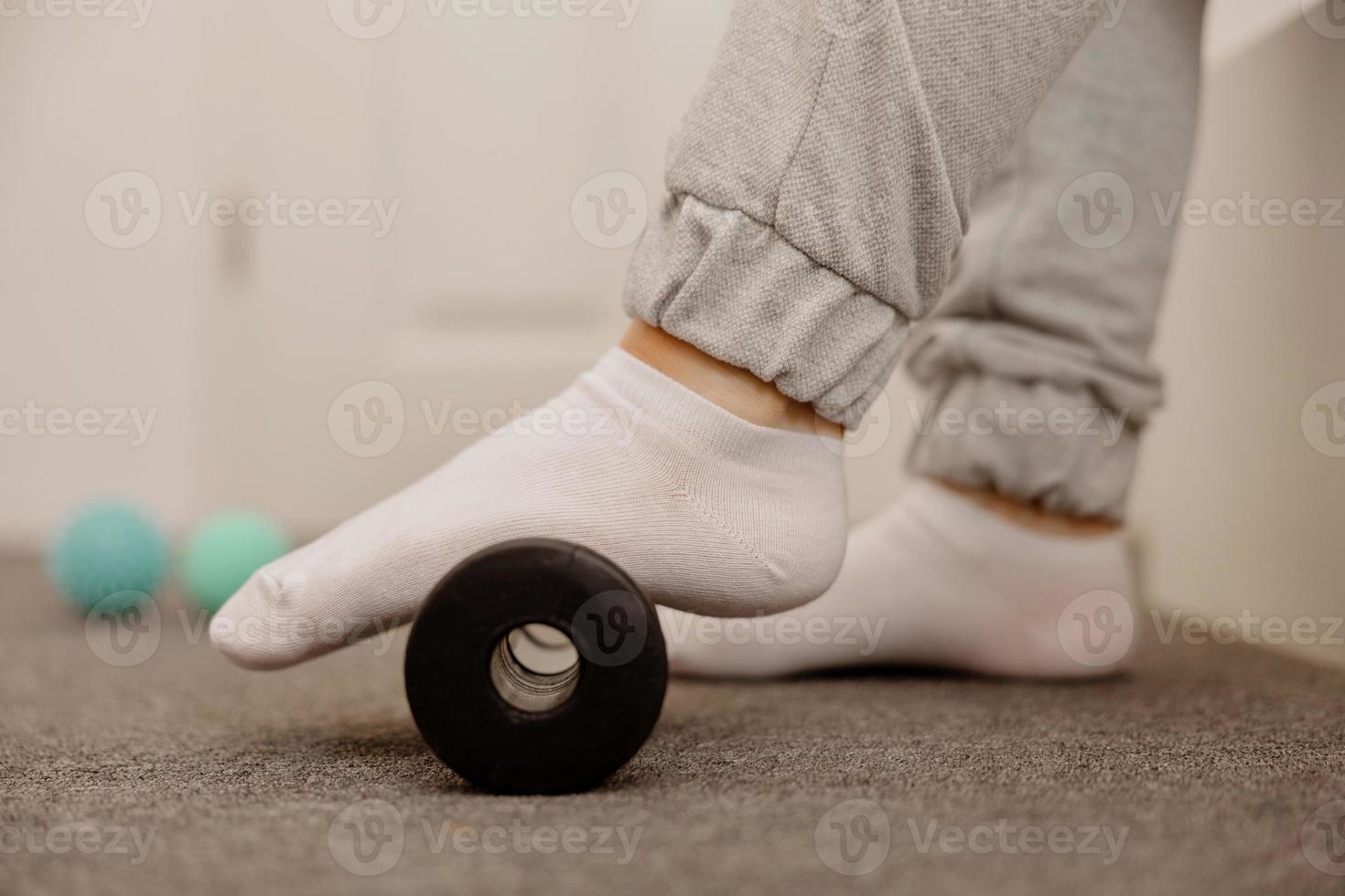 Woman doing flatfoot correction gymnastic exercise using massage roller. Myofascial relaxation of foot muscles. Hallux valgus. Pain. Identification of flat feet. Self care practices at home, health. photo
