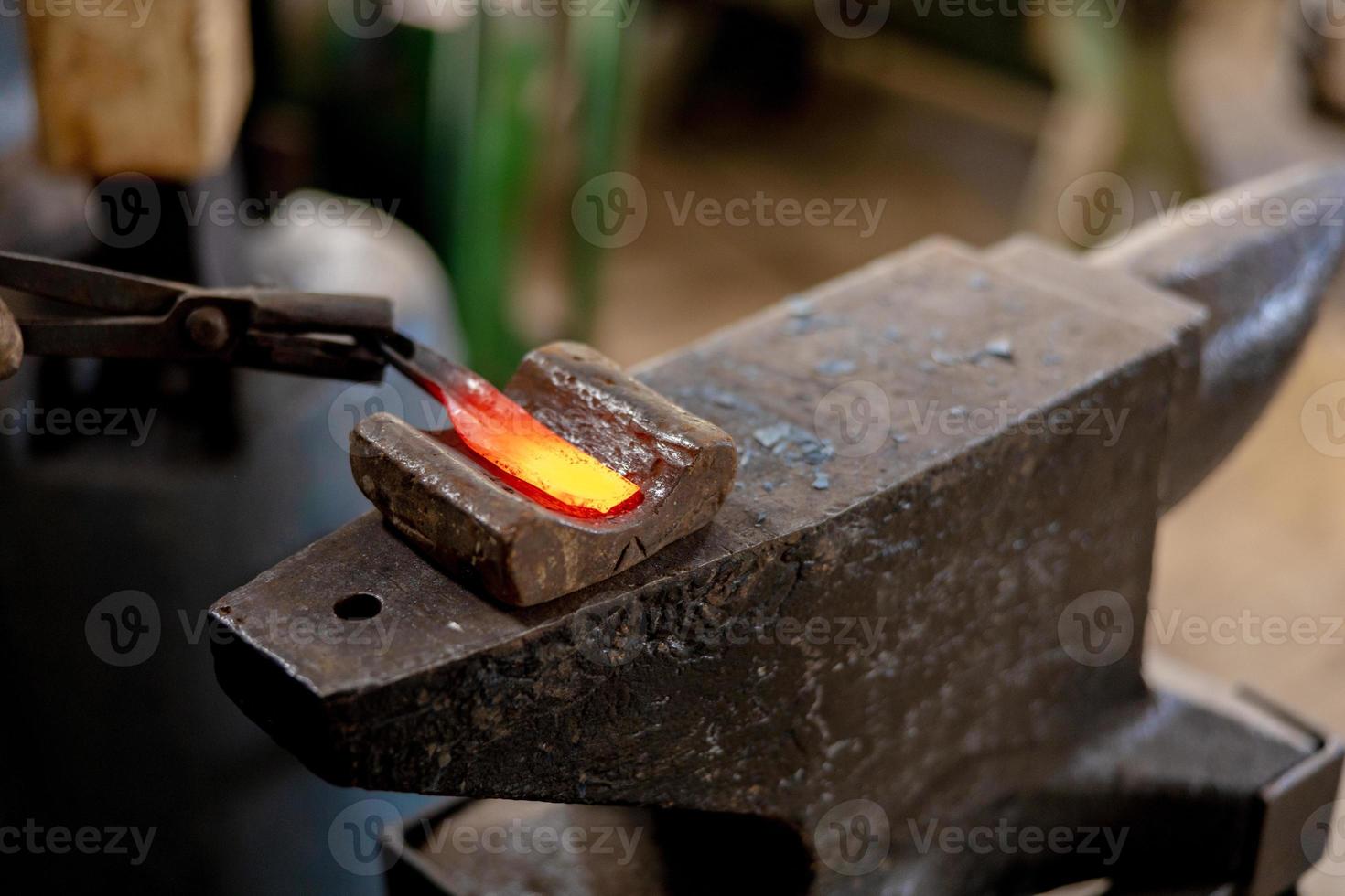 Close up view of heated metal and anvil. The blacksmith in the production process of metal products handmade in the forge. Blacksmith forging metal with a hammer. Metal industry, old profession. photo