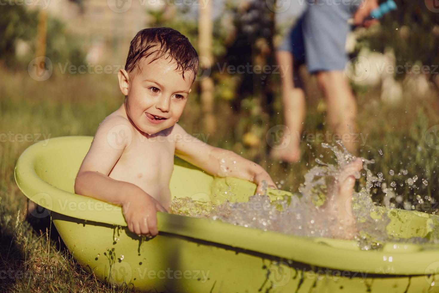 Cute little boy bathing in tub outdoors in garden. Happy child is splashing, playing with water and having fun. Summer season and recreation. Staying cool in the summer heat. Water fun in backyard. photo