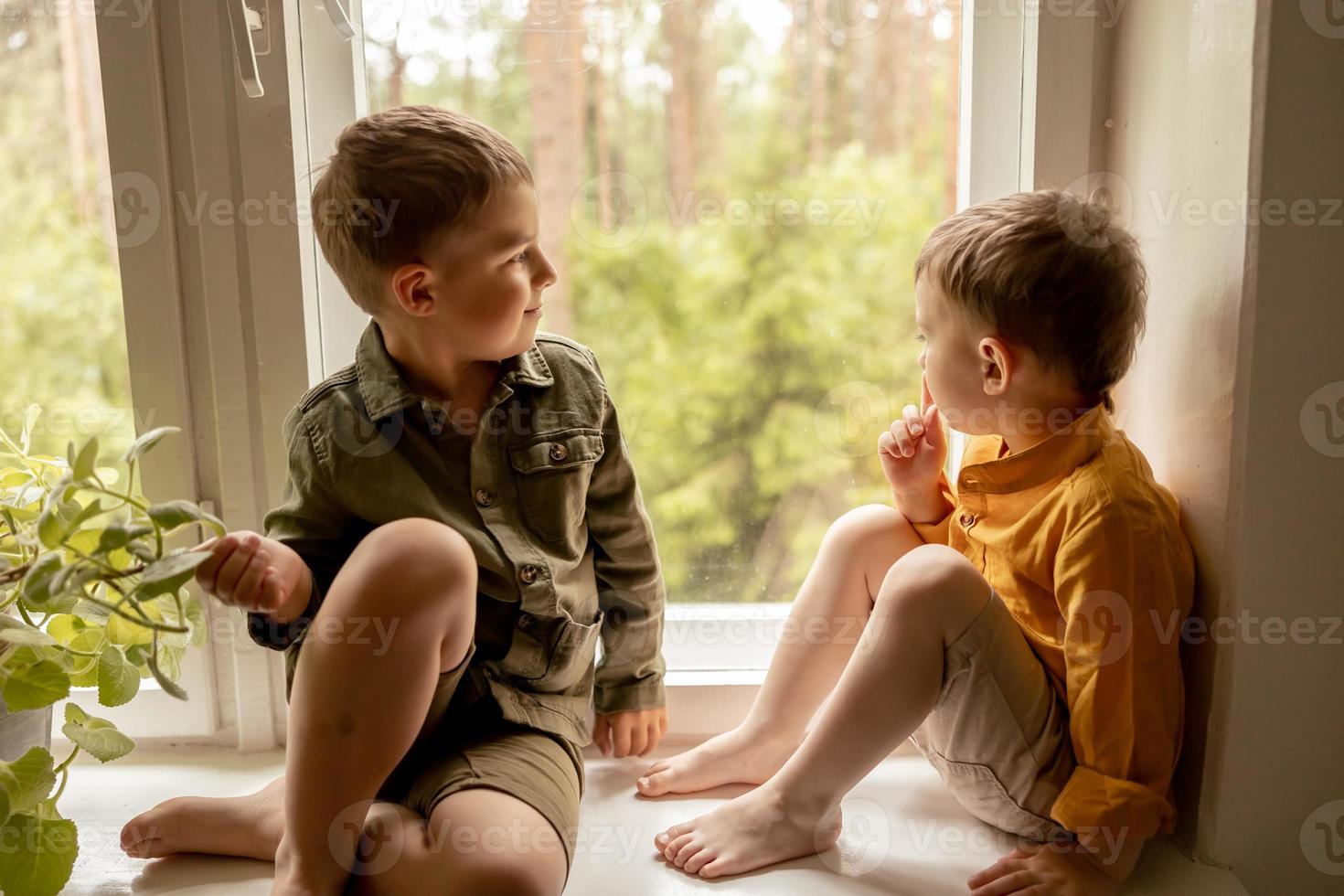 Children sitting on windowsill and waiting for someone comming. Two brothers, friends. Cute preschool kids alone at home. Boys are waiting for their mother or father. Loneliness. Busy parents. photo