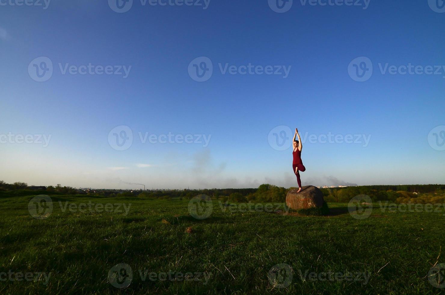 Silhouette of young blonde girl in sport suit practice yoga on a picturesque green hill in the evening at sunset. The concept of exercising and healthy lifestyles photo