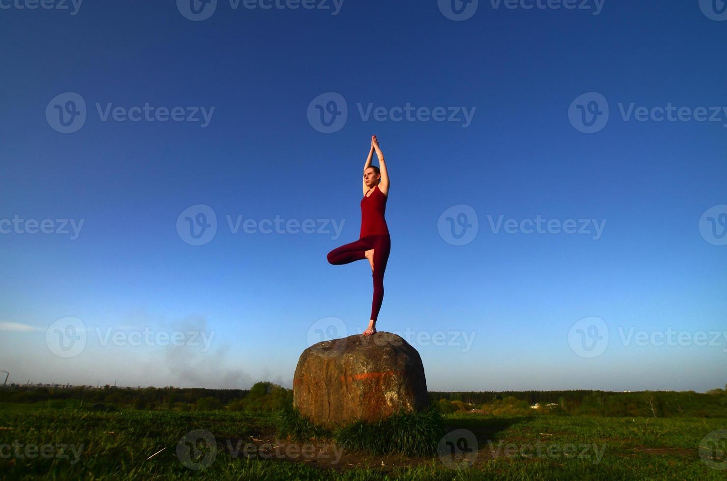 la silueta de una joven rubia con traje deportivo practica yoga en una pintoresca colina verde por la noche al atardecer. el concepto de ejercicio y estilos de vida saludables foto