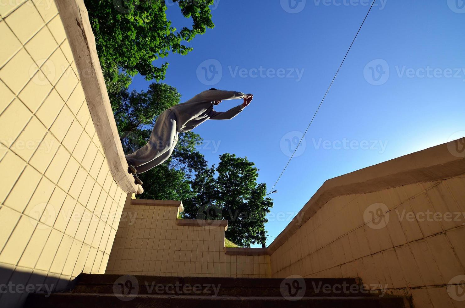 un chico joven realiza un salto a través del espacio entre los parapetos de hormigón. el atleta practica parkour, entrenando en condiciones de calle. vista inferior foto