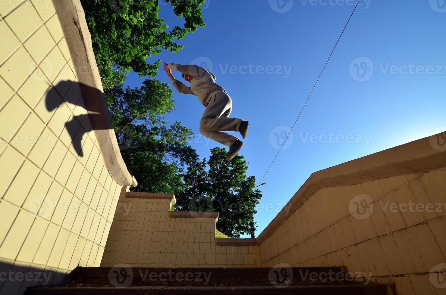 un chico joven realiza un salto a través del espacio entre los parapetos de hormigón. el atleta practica parkour, entrenando en condiciones de calle. vista inferior foto