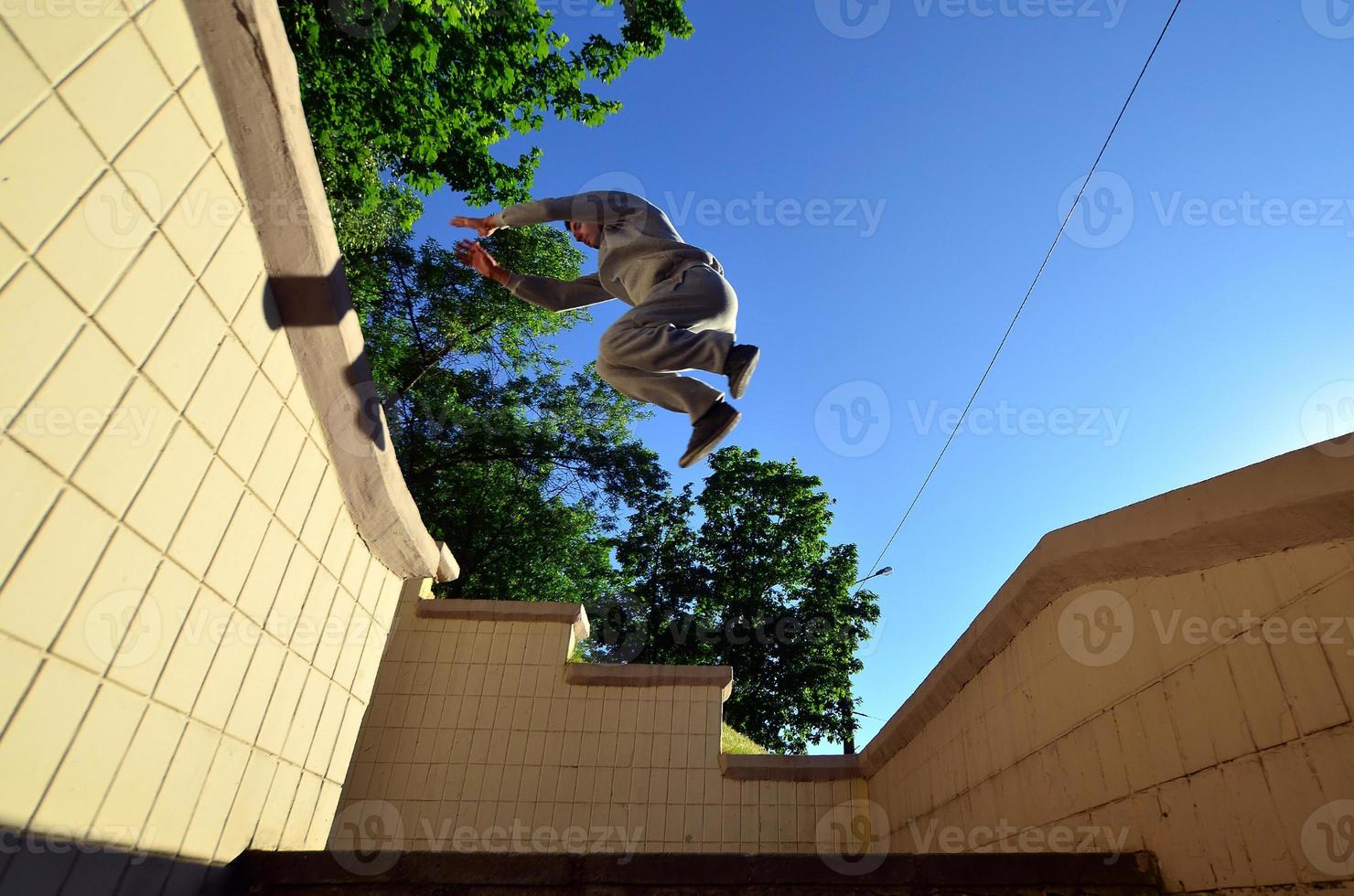 A young guy performs a jump through the space between the concrete parapets. The athlete practices parkour, training in street conditions. Bottom view photo